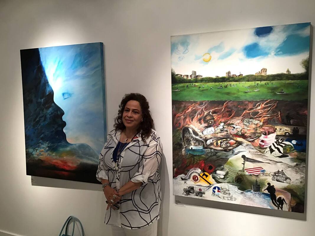 A person poses between two paintings hanging on a wall. One painting shows an abstract shape suggesting a face and bold brushstrokes of light and color. The other depicts a city park full of people, while representations of war are visible underground. 