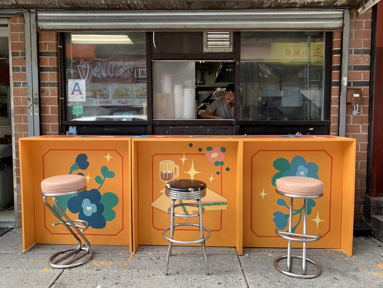 A dining counter in front of a Chinatown restaurant, painted bright orange with floral and food motifs.