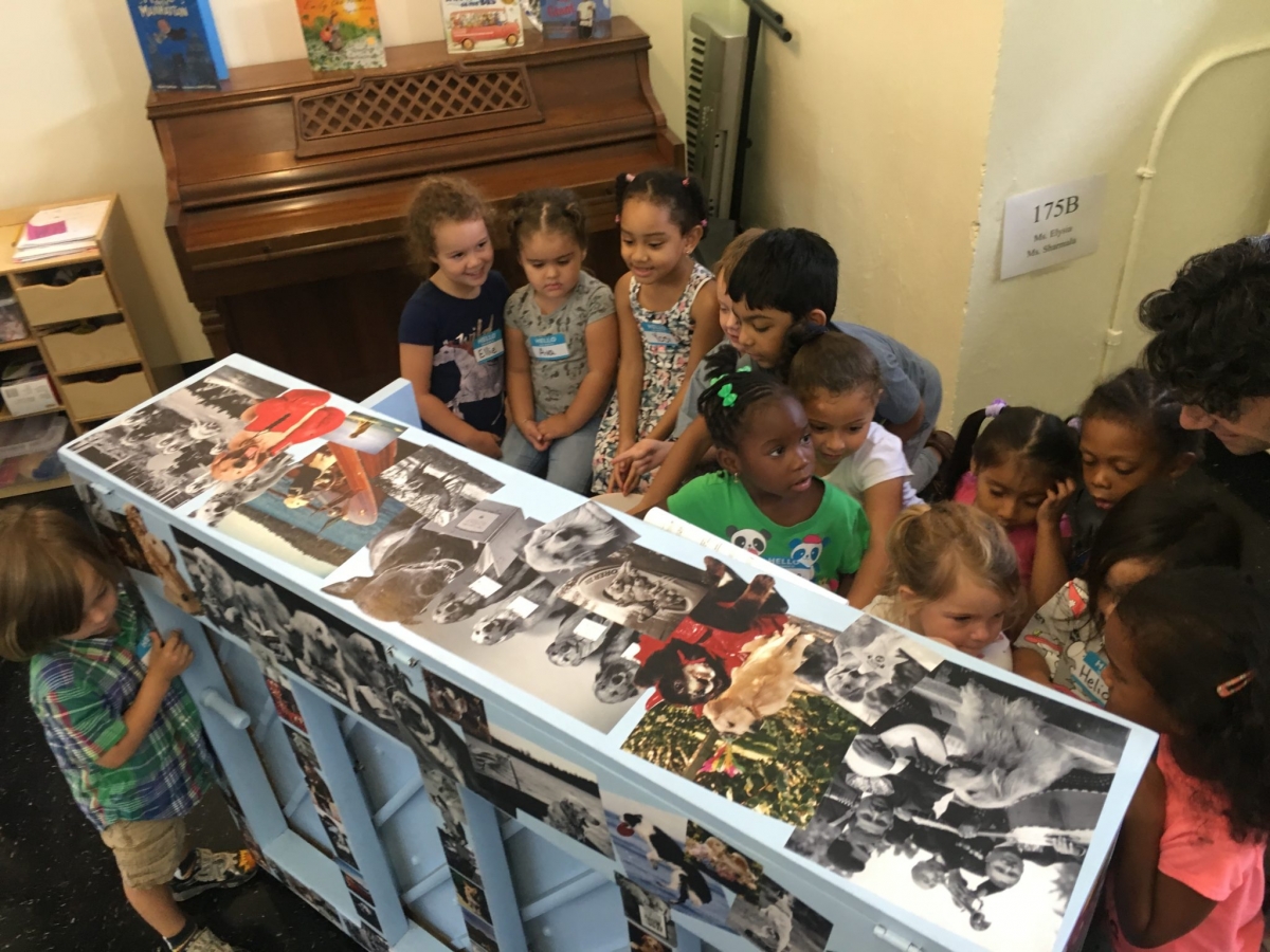 Young students sit around a white piano decorated with photos of dogs